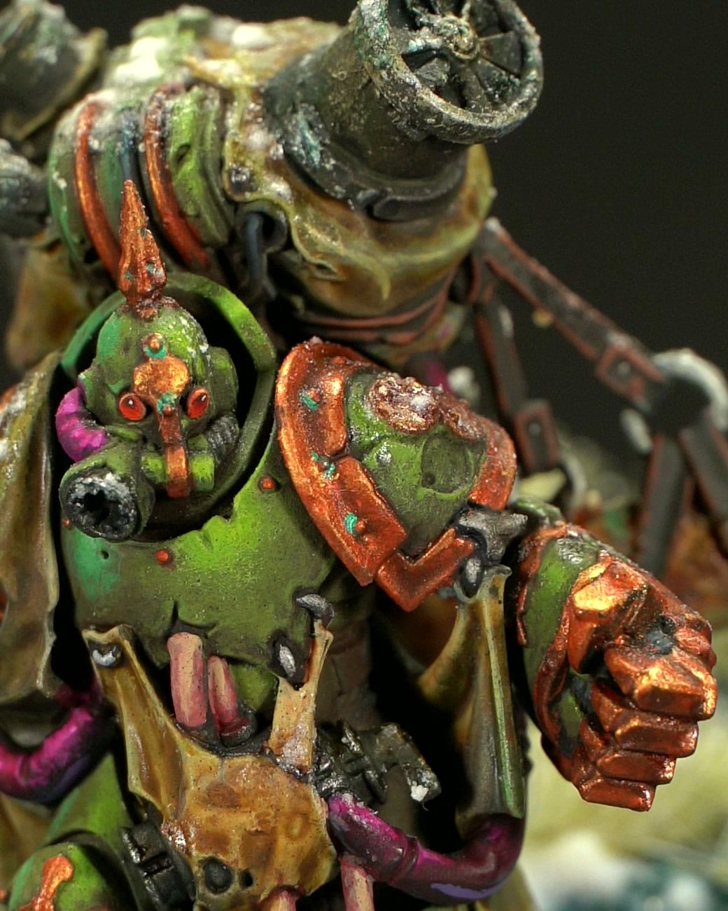 Gros plan sur le casque, l’épaulière et le poing : armure verte aux bordures cuivrées et lentilles rouges