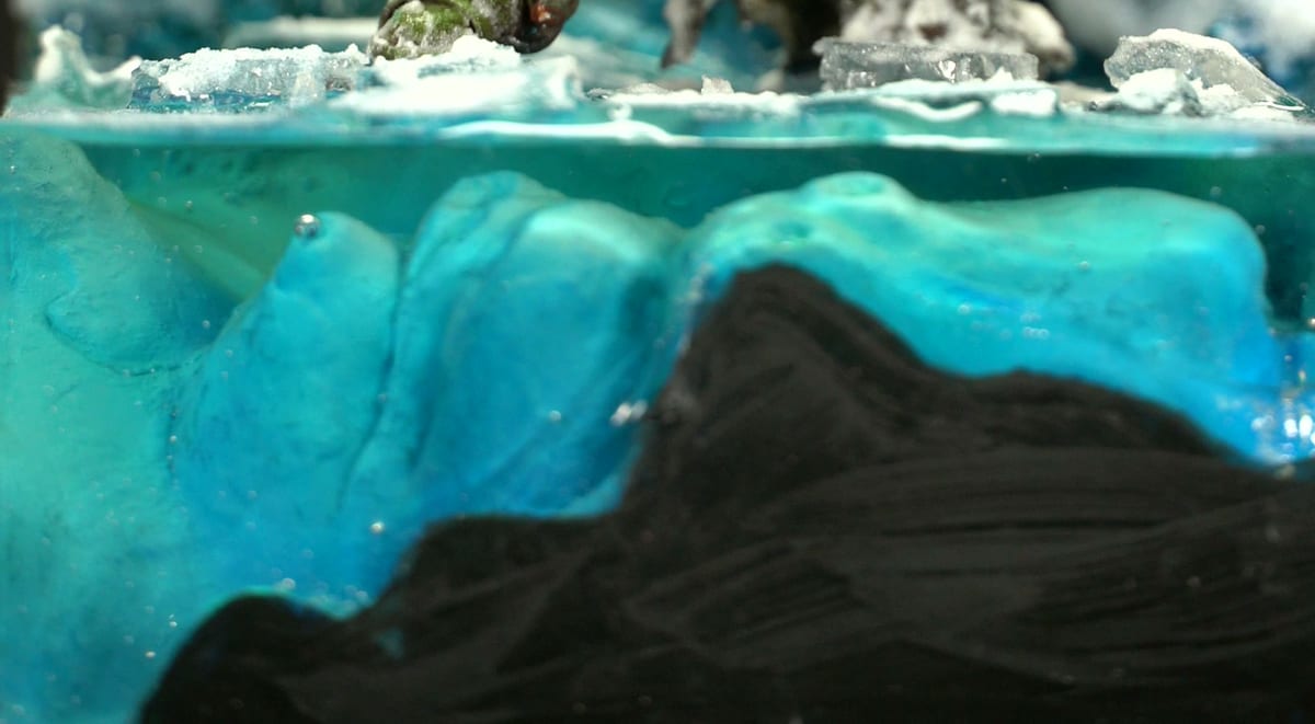 Vue latérale du socle : glace bleue translucide sur roche sombre, avec des plaques de glace brisées au-dessus
