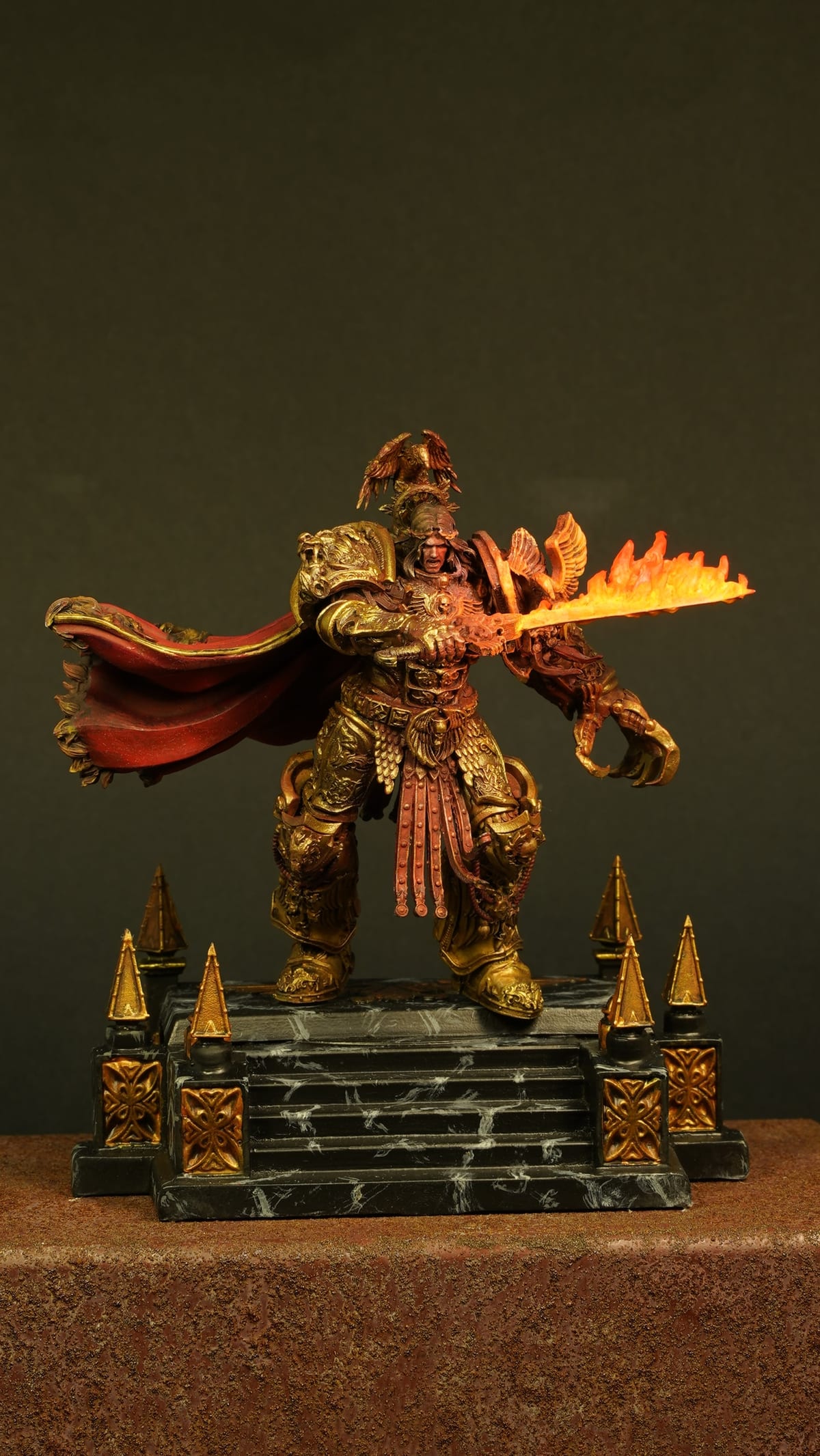 A warrior in gold and red holding a flaming sword, on a spiked golden base