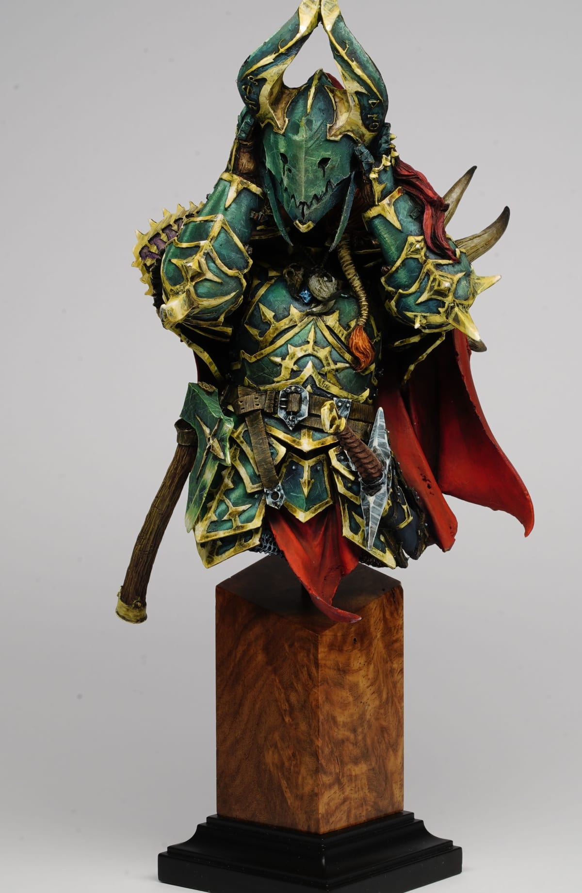Bust in ornate green armour with a red cloak, on a wooden plinth
