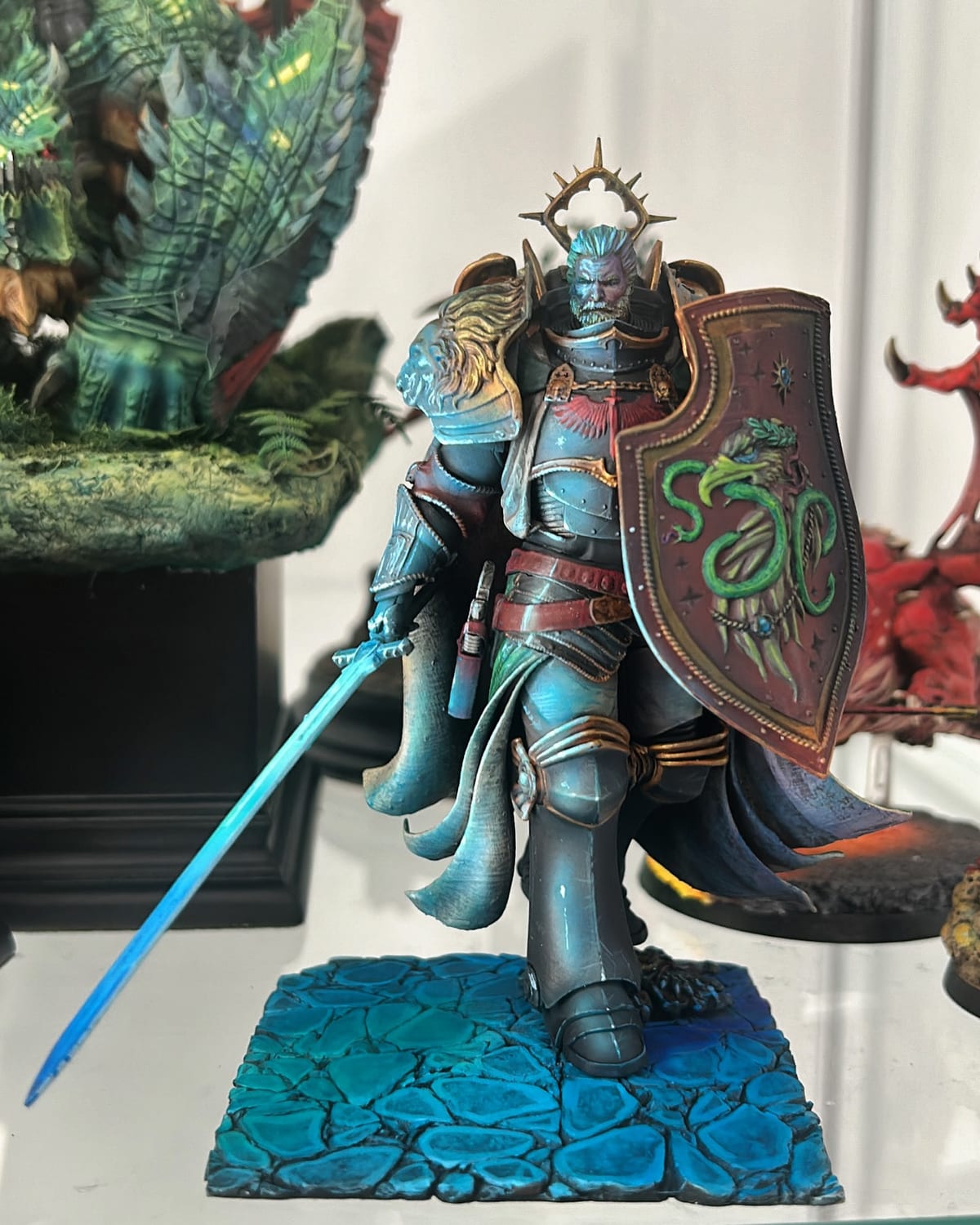 Lion El’Jonson con una espada azul brillante y un escudo, sobre una peana de piedra