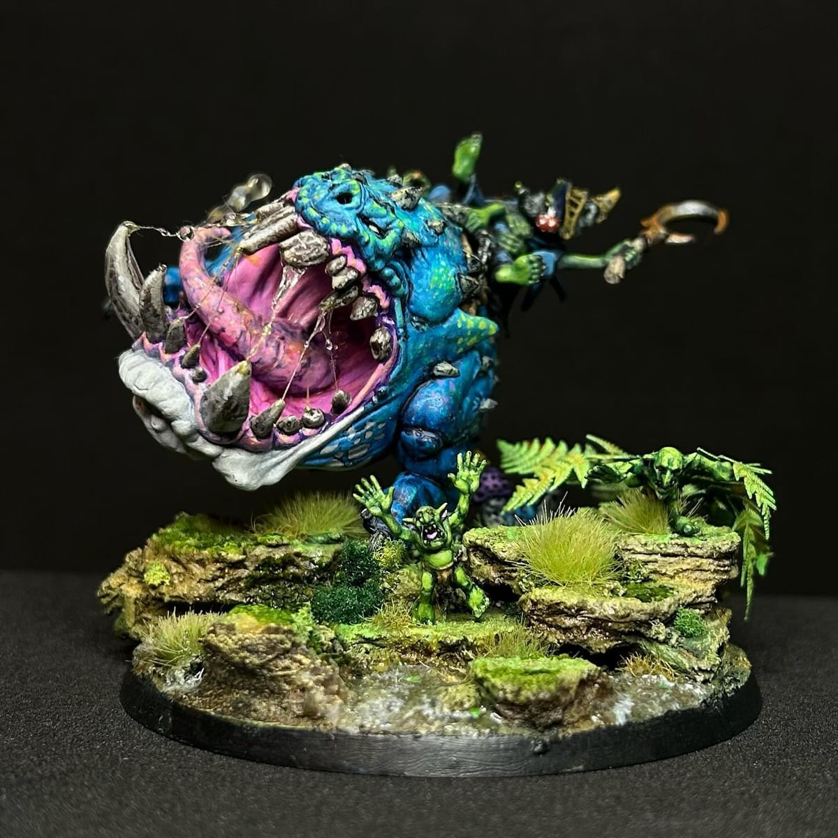 Un squig azul con manchas y una boca rosa abierta de par en par, entre helechos y musgo