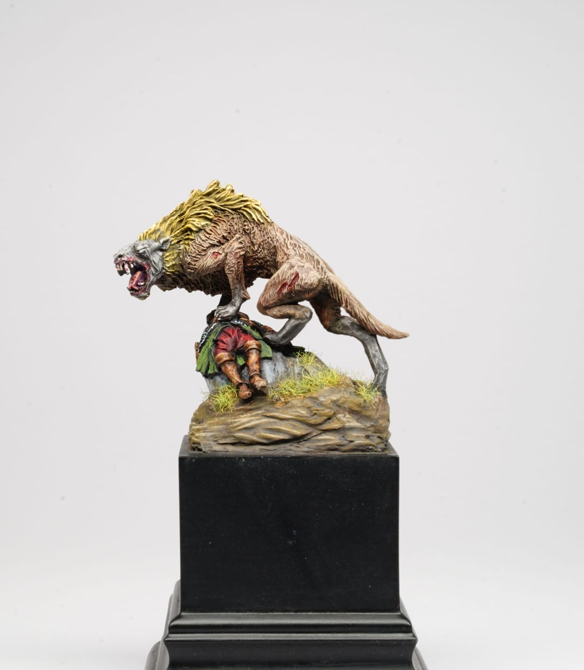 A warg with a yellow mane and open jaws standing over a fallen warrior on a rocky base